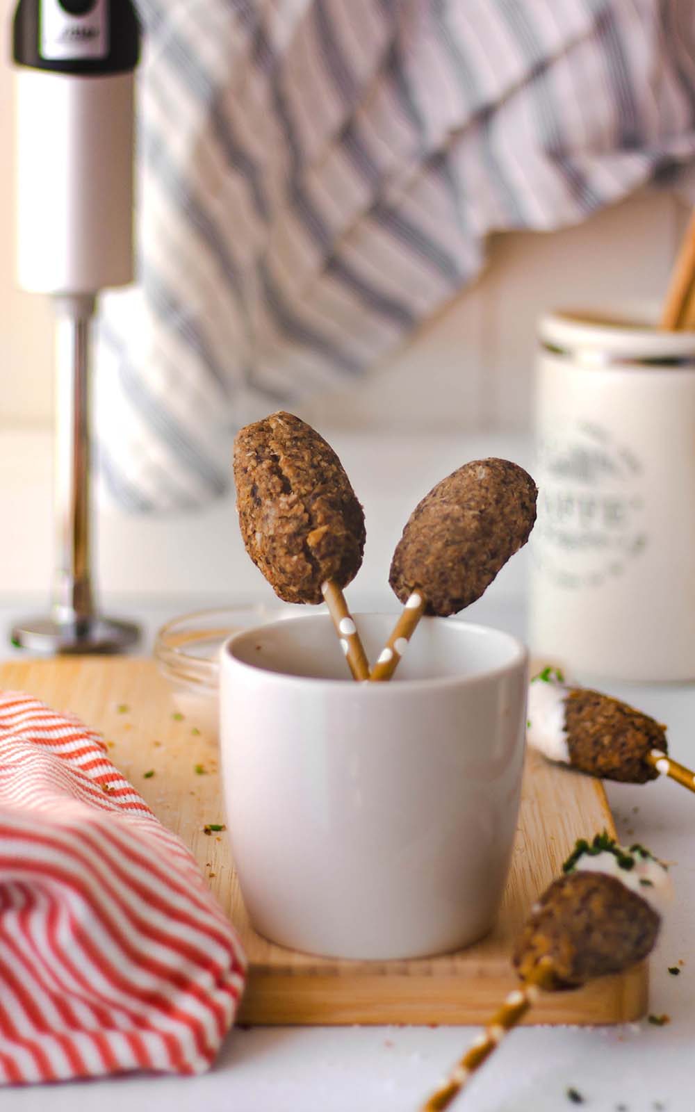 Champignon Party-Frikadellen auf kleinen Sticks serviert, in einer weißen Tasse angerichtet. Im Hintergrund sind Küchenutensilien und ein ritter Stabmixer zu sehen Champignon Party-Frikadellen auf kleinen Sticks serviert, in einer weißen Tasse angerichtet. Im Hintergrund sind Küchenutensilien und ein ritter Stabmixer zu sehen