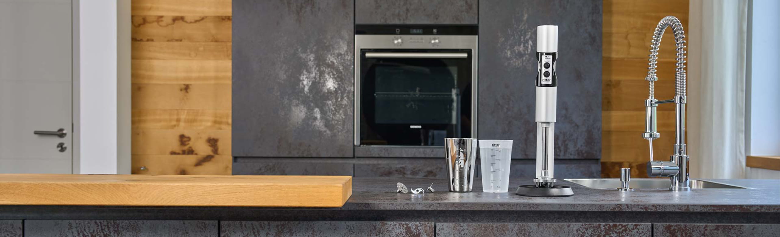 A picture of a silver hand blender and two measuring jugs standing on a kitchen worktop.