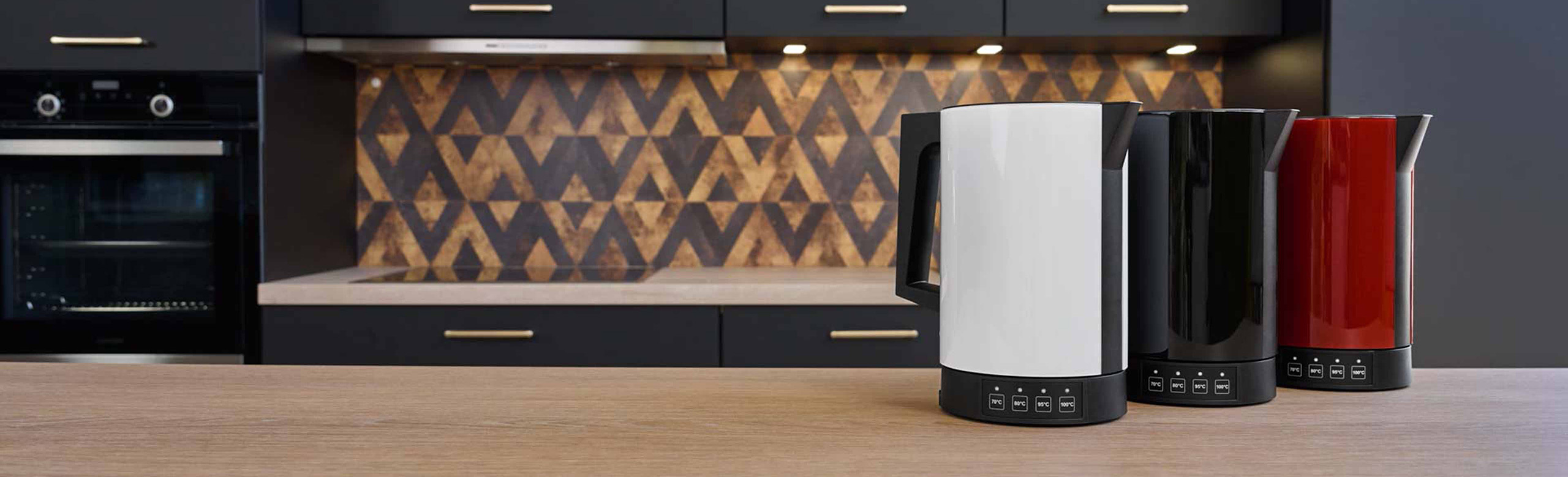 Ein Bild von einem roten, einem schwarzen und einem weißen Wasserkocher die nebeneinander auf einer Küchenplattform stehen.