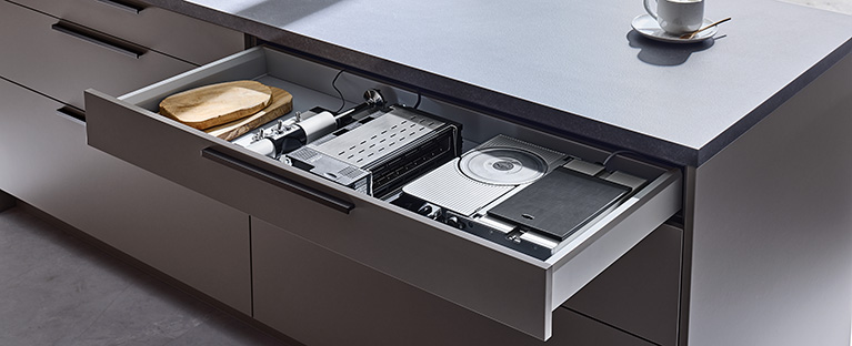 Ein Bild von einer Einbaukombination bestehend aus einem Einbau-Toaster, einem Einbau-Stabmixer und einem Einbau-Allesschneider, die eingeklappt in einer Küchenschublade liegen.