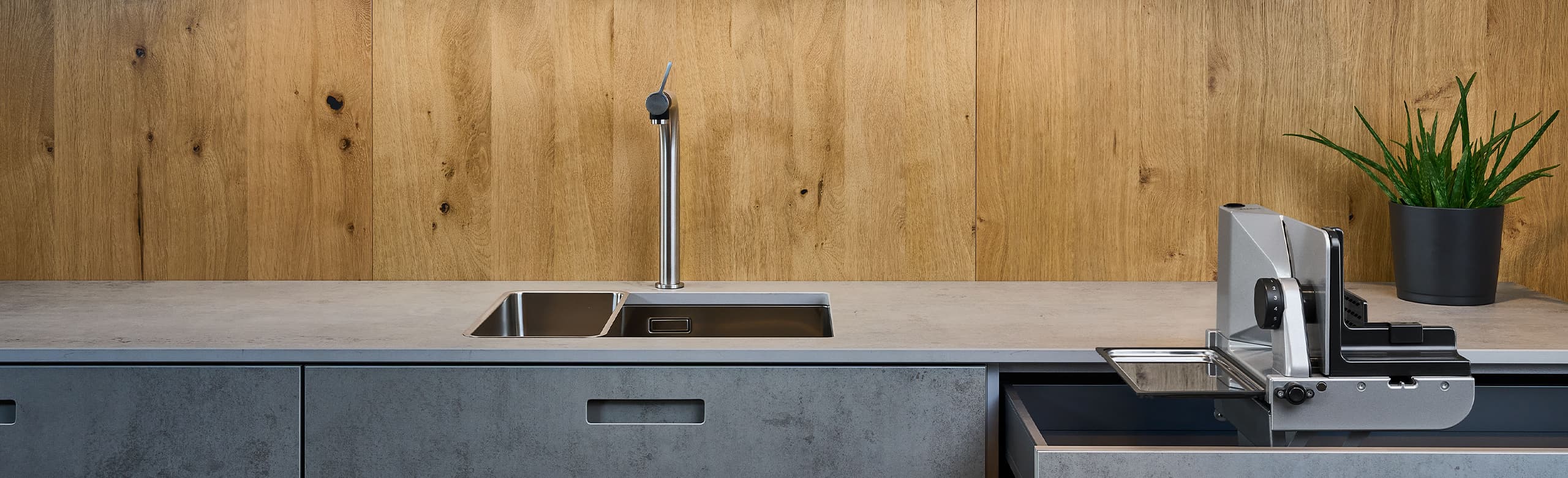 A picture of a built-in all-purpose slicer emerging from a kitchen drawer and a plant standing on the worktop.