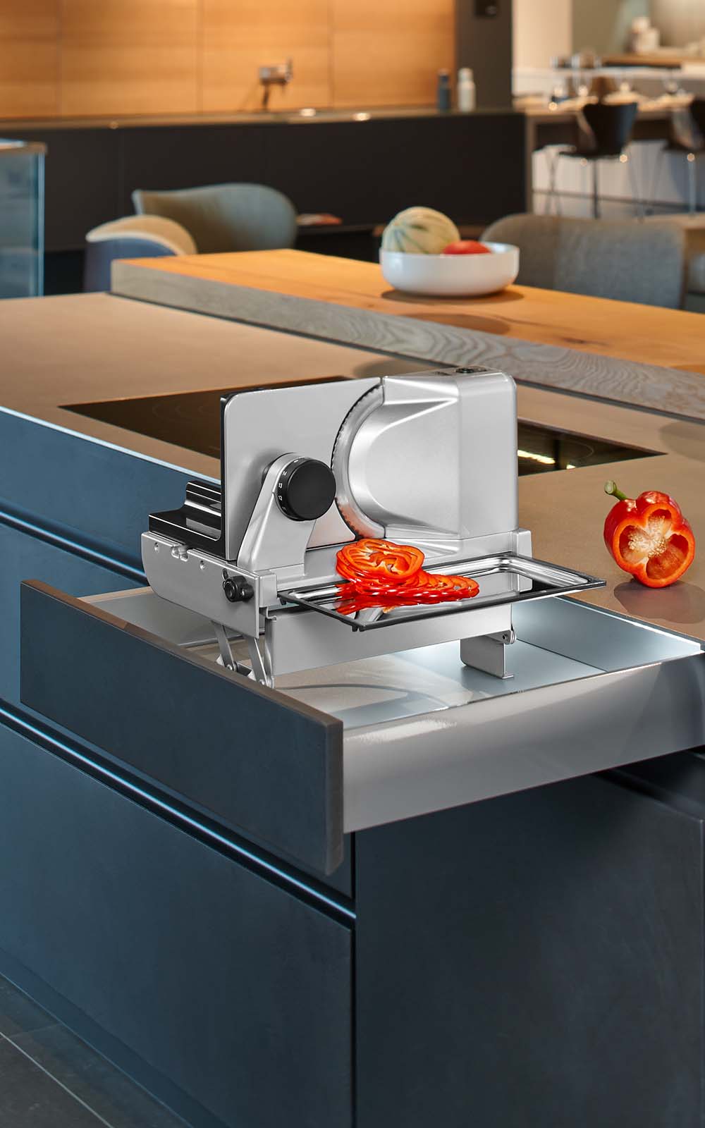 A picture of a built-in food slicer emerging from a kitchen drawer and slicing ham. A picture of a built-in food slicer emerging from a kitchen drawer and slicing ham.