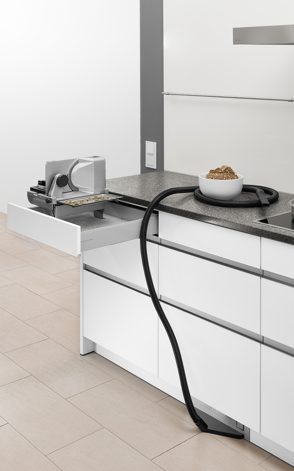 Ein Bild von einer Einbaukombination in einer Küche, die aus einem Einbau-Sockelsauger und einem linksgeführten und aufgestellten Einbau-Allesschneider besteht. Ein Bild von einer Einbaukombination in einer Küche, die aus einem Einbau-Sockelsauger und einem linksgeführten und aufgestellten Einbau-Allesschneider besteht.