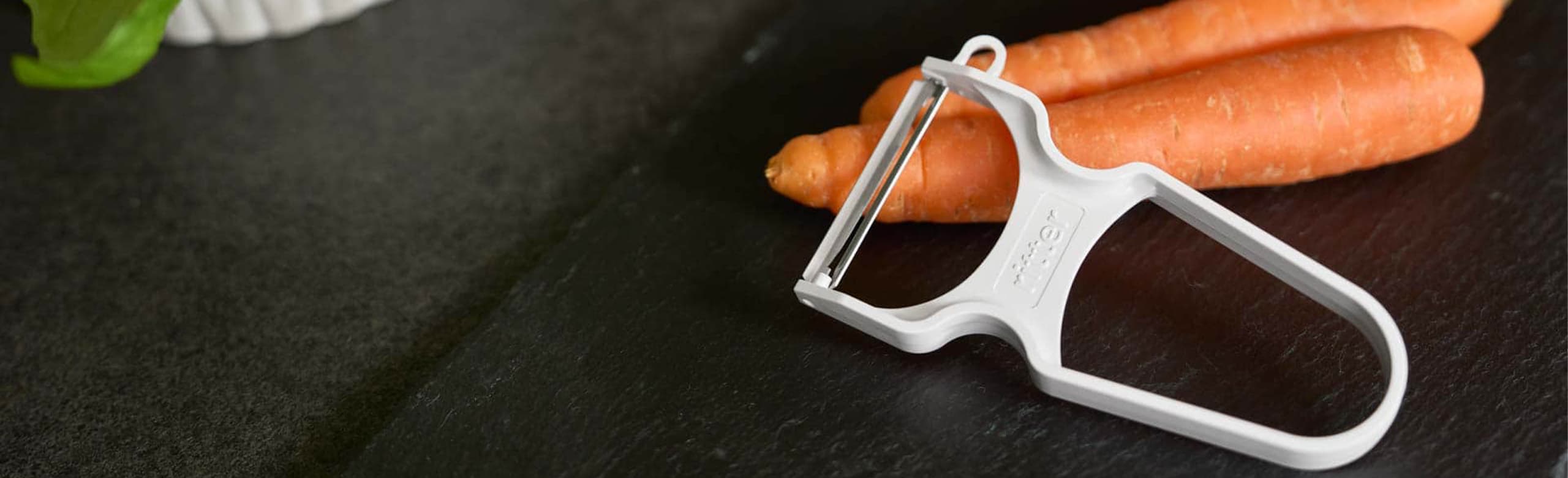 A picture of a peeler and carrots lying on a kitchen worktop.