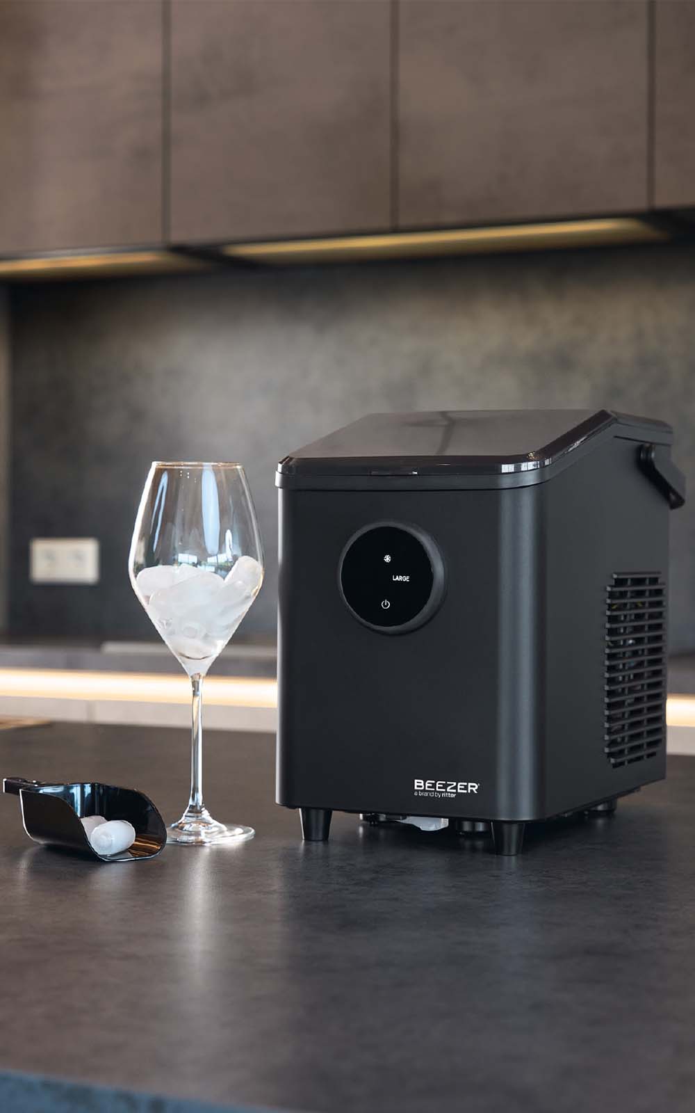 Schwarze Eiswürfelmaschine daneben ein Glas mit Eiswürfel befüllt und eine kleine schwarze Eiswürfelschaufel.