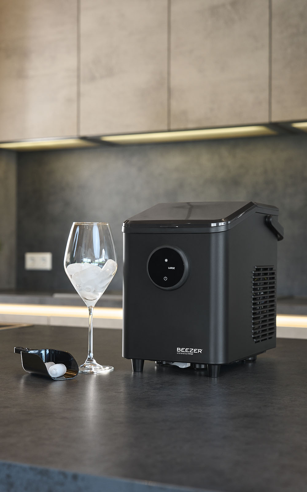 Schwarze Eiswürfelmaschine daneben ein Glas mit Eiswürfel befüllt und eine kleine schwarze Eiswürfelschaufel.