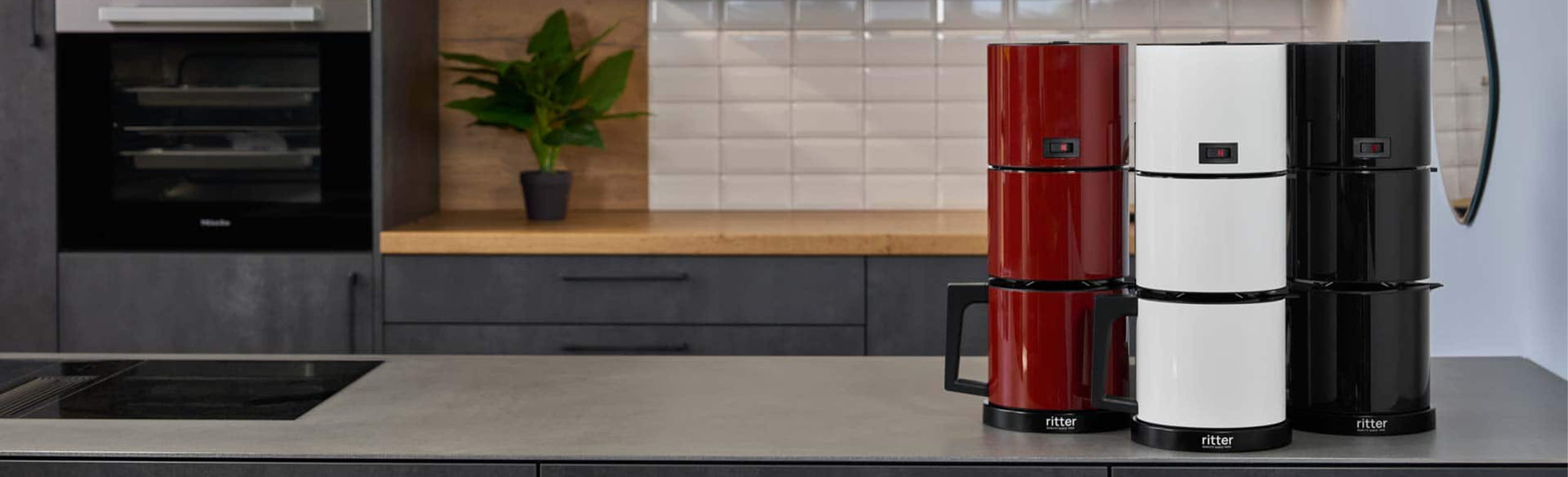 A picture of a red, a black and a white coffee machine standing next to each other on a kitchen platform.