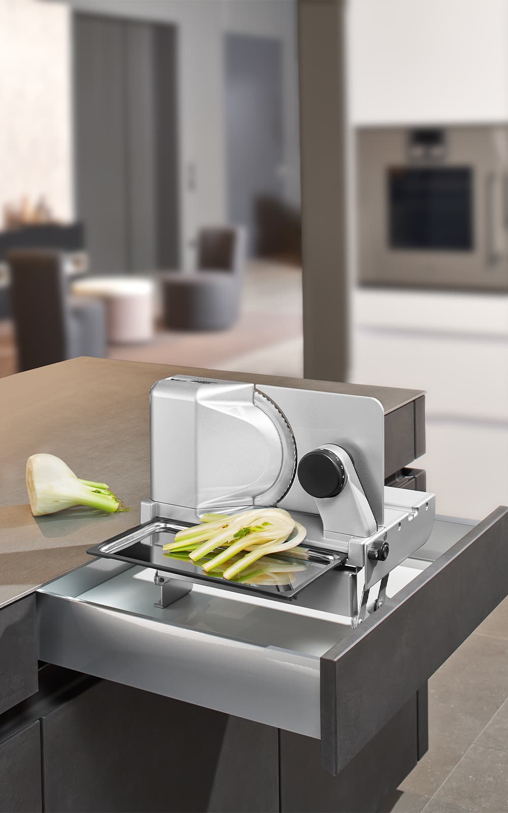 A picture of a built-in food slicer emerging from a kitchen drawer and slicing vegetables. A picture of a built-in food slicer emerging from a kitchen drawer and slicing vegetables.