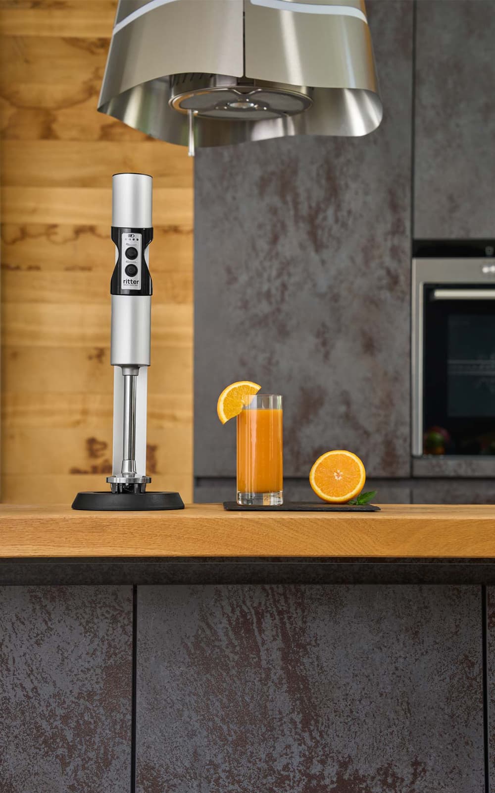 A picture of a silver hand blender standing next to a glass of orange juice in a kitchen. A picture of a silver hand blender standing next to a glass of orange juice in a kitchen.