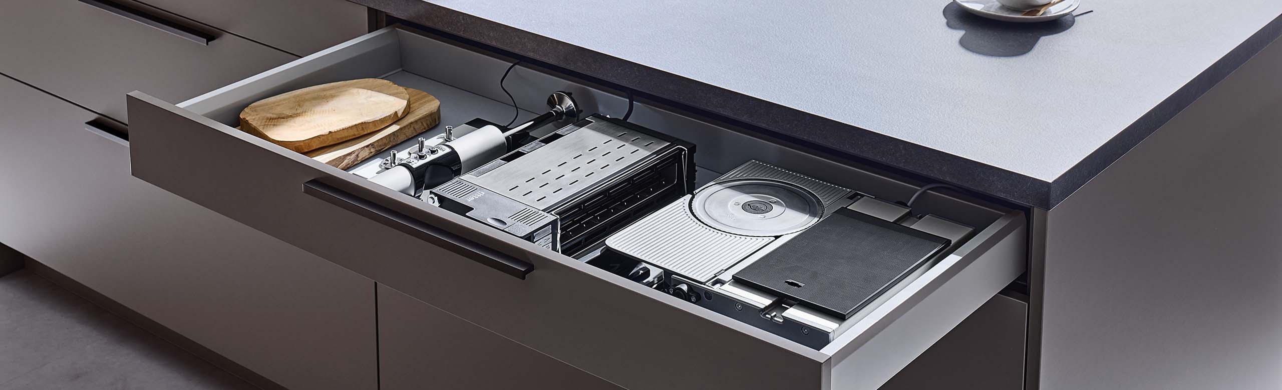 Ein Bild von einer Einbaukombination bestehend aus einem Einbau-Toaster, einem Einbau-Stabmixer und einem Einbau-Allesschneider, die eingeklappt in einer Küchenschublade liegen.