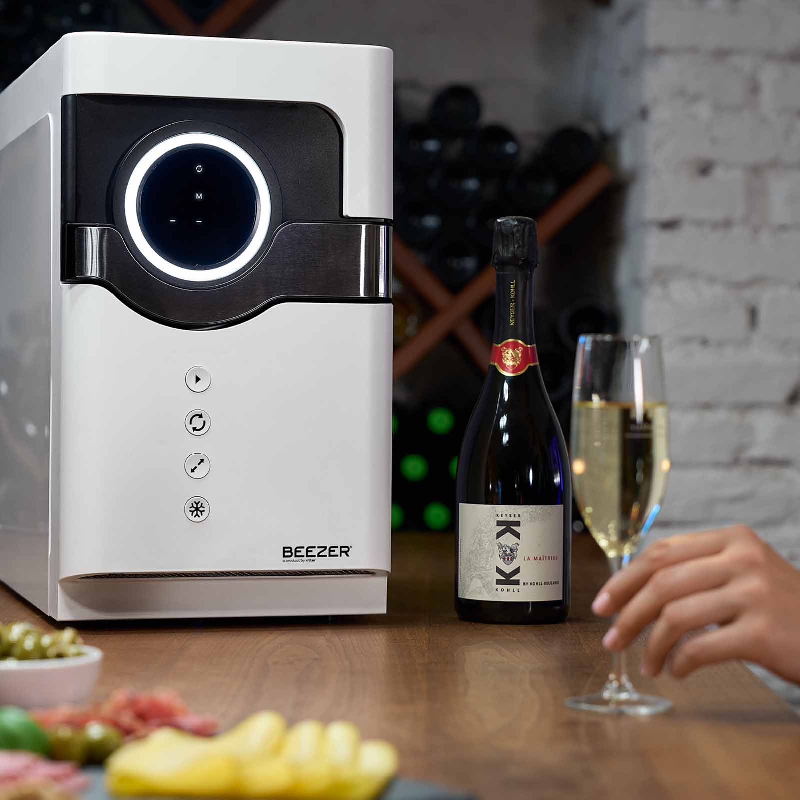A picture of the white BEEZER drinks cooler, with a wine bottle and a wine glass standing next to the BEEZER in a wine cellar.