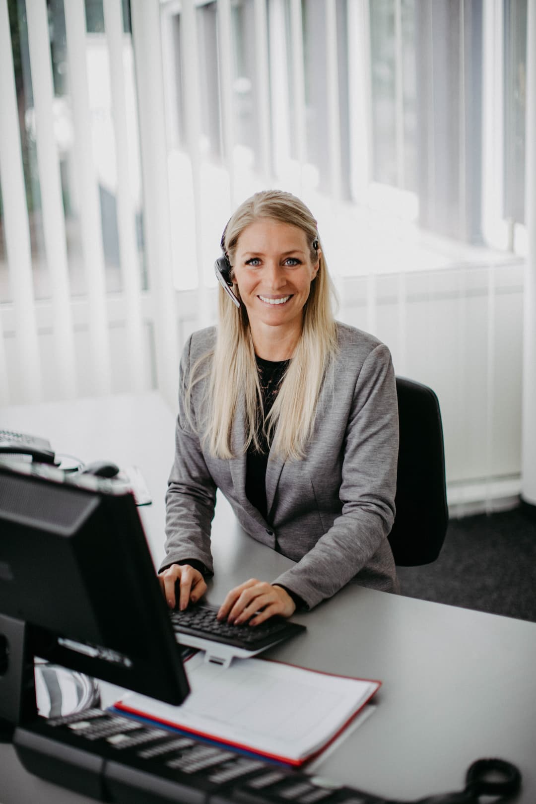 A picture of a blonde woman sitting at a computer with a headset and laughing. A picture of a blonde woman sitting at a computer with a headset and laughing.