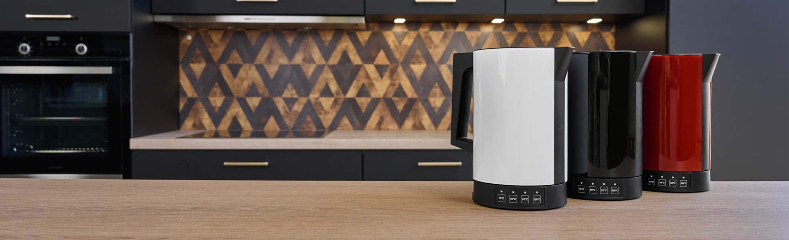 A picture of a red, a black and a white kettle standing next to each other on a kitchen platform.